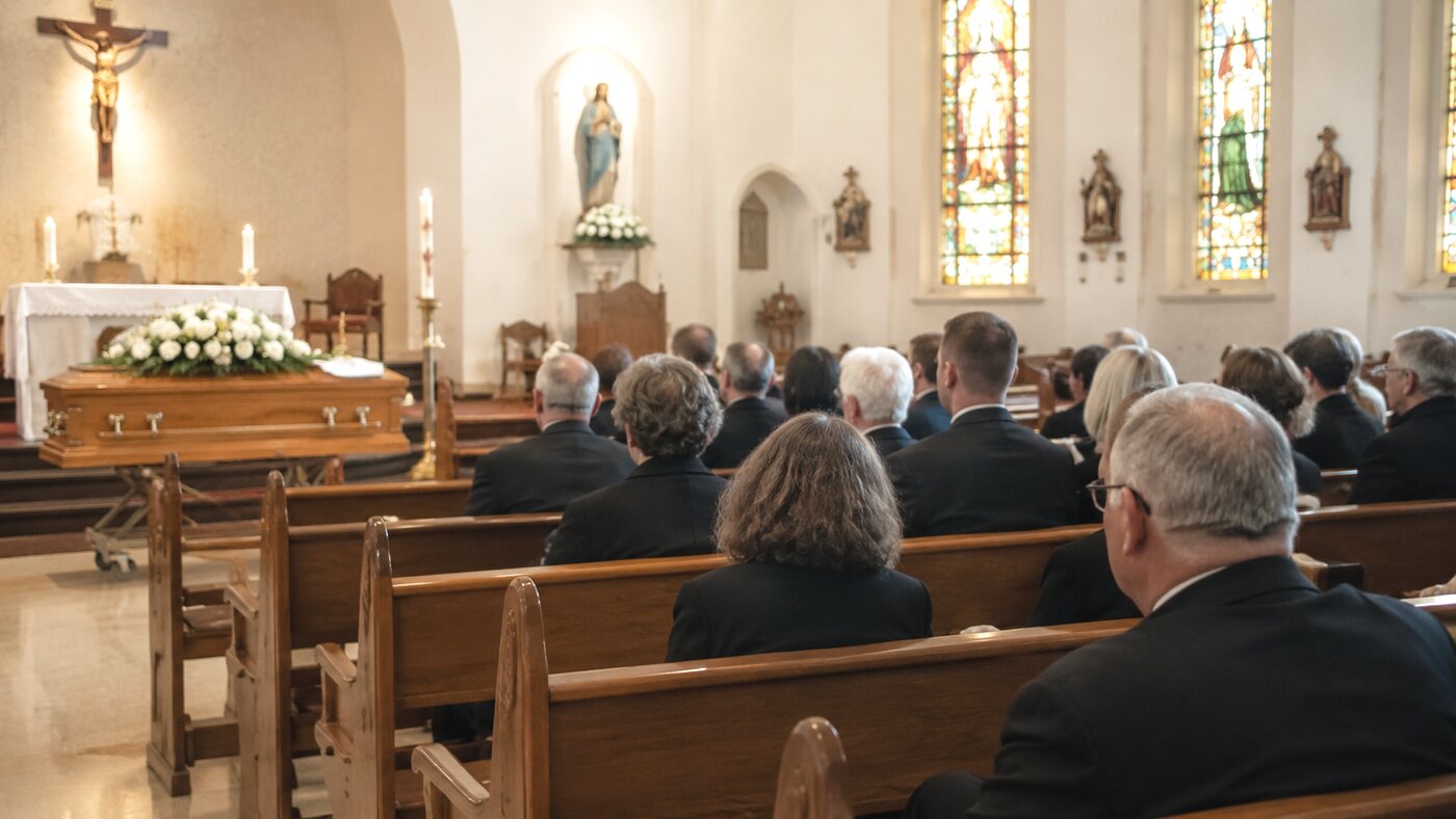 A Catholic funeral service in a church with statues and stained glass