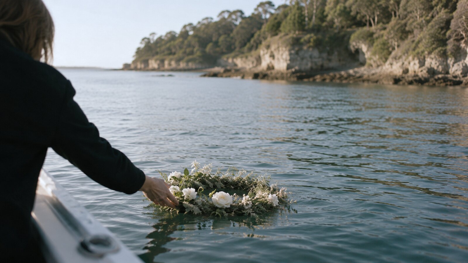 A hand lowering a floral wreath onto calm water